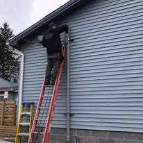Technician on ladder installing equipment on building exterior